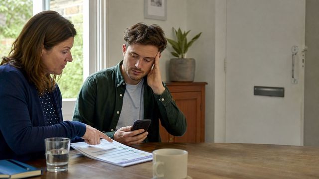 Two people reviewing a safety plan and phone at a kitchen table during a calm support conversation